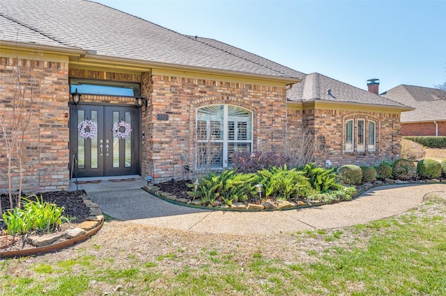 entrance to property with french doors, brick siding, and a shingled roof