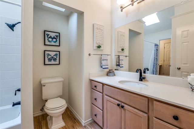 full bathroom with toilet, wood finished floors, a skylight, baseboards, and vanity