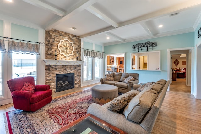 living area with beam ceiling, a stone fireplace, coffered ceiling, and wood finished floors