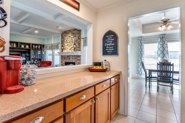 kitchen with light tile patterned floors, a healthy amount of sunlight, brown cabinets, and light stone countertops