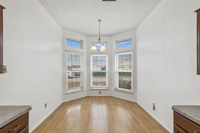 unfurnished dining area featuring visible vents, baseboards, an inviting chandelier, a textured ceiling, and light wood-type flooring