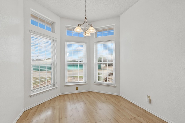 unfurnished dining area with a textured ceiling, baseboards, wood finished floors, and a notable chandelier