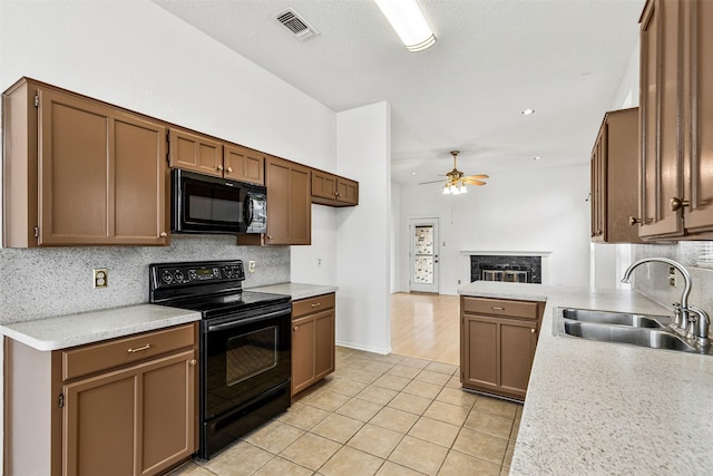 kitchen featuring a fireplace, visible vents, decorative backsplash, a sink, and black appliances