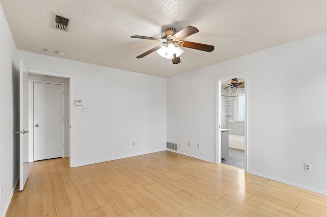 empty room with light wood-style floors, baseboards, visible vents, and a textured ceiling