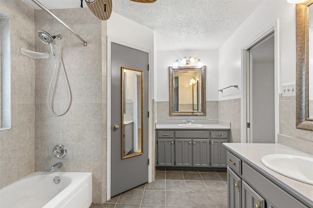 full bath with a textured ceiling, shower / tub combination, a sink, two vanities, and tile walls