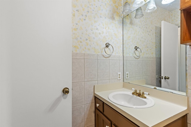 bathroom with wallpapered walls, a wainscoted wall, tile walls, and vanity