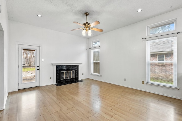 unfurnished living room featuring a wealth of natural light, a high end fireplace, ceiling fan, and wood finished floors