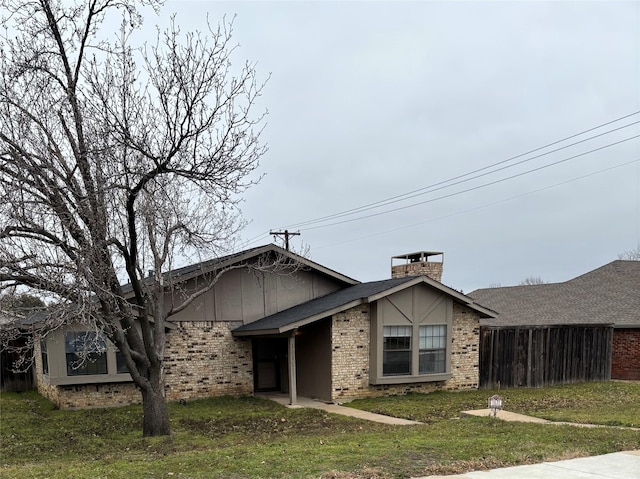 view of front of property with a front yard, brick siding, fence, and a chimney