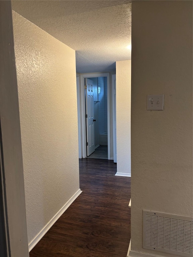 corridor with dark wood finished floors, visible vents, a textured wall, and a textured ceiling