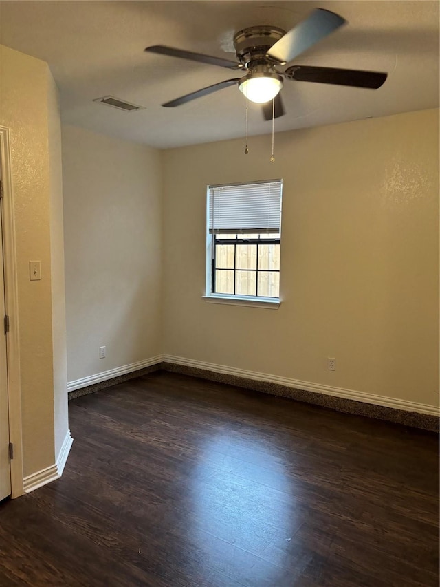 empty room featuring dark wood-type flooring, a ceiling fan, visible vents, and baseboards