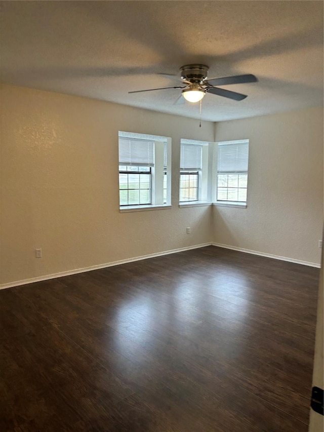 empty room featuring a ceiling fan, a textured ceiling, baseboards, and dark wood-type flooring