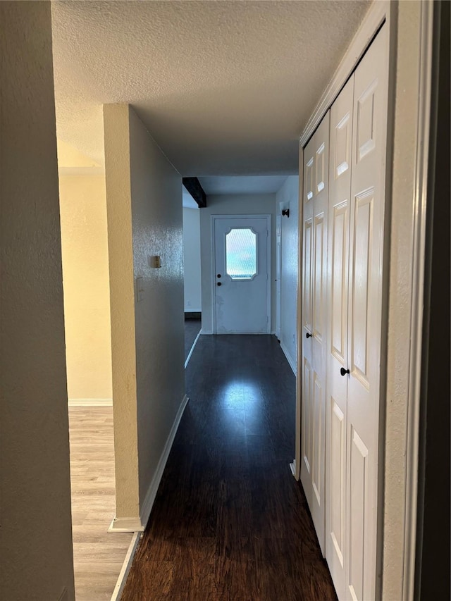 corridor with a textured ceiling, baseboards, wood finished floors, and a textured wall