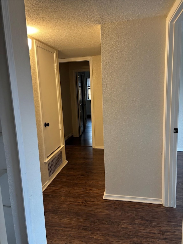 hall with baseboards, visible vents, a textured wall, dark wood-style flooring, and a textured ceiling