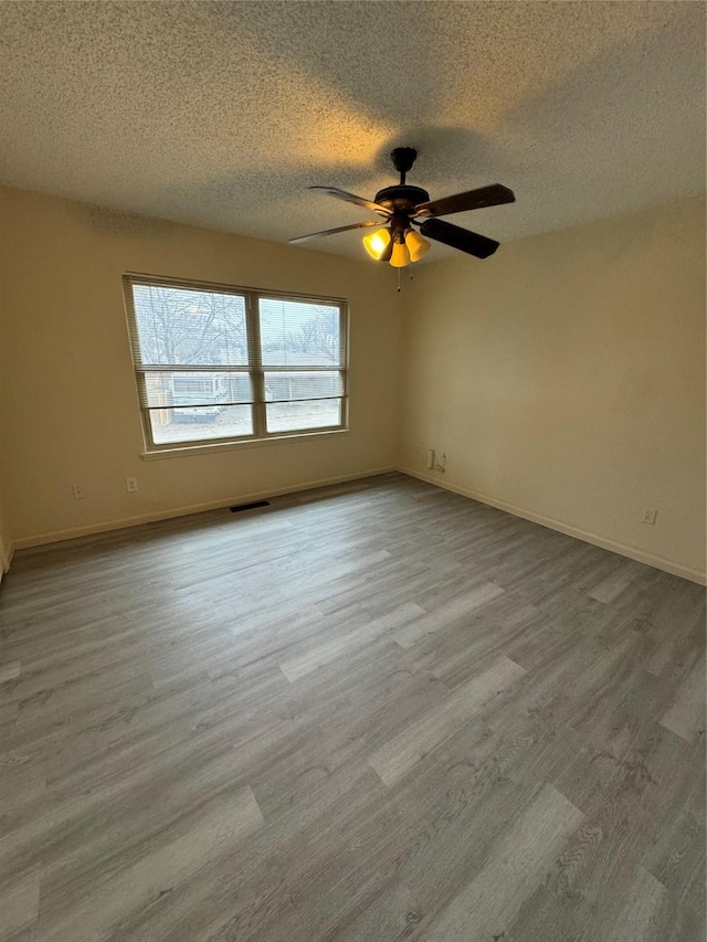 spare room featuring a textured ceiling, wood finished floors, visible vents, and baseboards