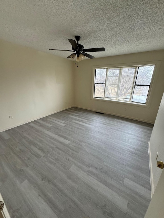 spare room featuring a textured ceiling, wood finished floors, visible vents, and baseboards