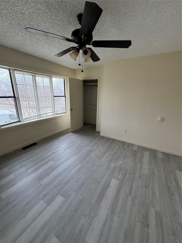 unfurnished bedroom with baseboards, a textured ceiling, visible vents, and wood finished floors