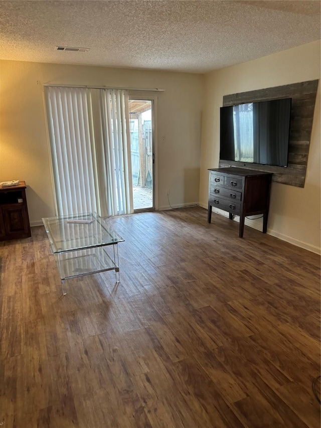 unfurnished living room with a textured ceiling, wood finished floors, visible vents, and baseboards