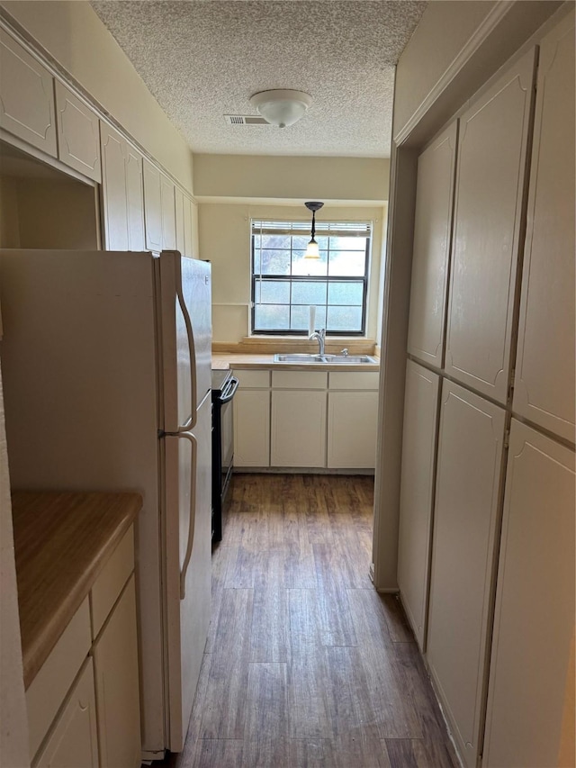 kitchen featuring white cabinets, black range with electric stovetop, wood finished floors, freestanding refrigerator, and a sink