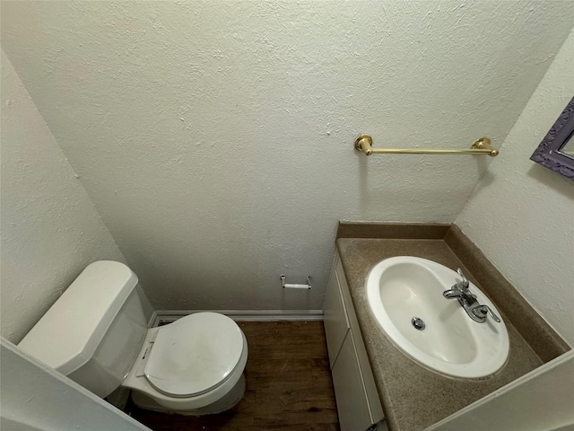 half bathroom with a textured wall, wood finished floors, vanity, and toilet