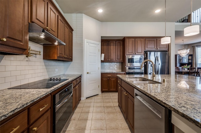 kitchen featuring stone countertops, a sink, stainless steel appliances, under cabinet range hood, and pendant lighting