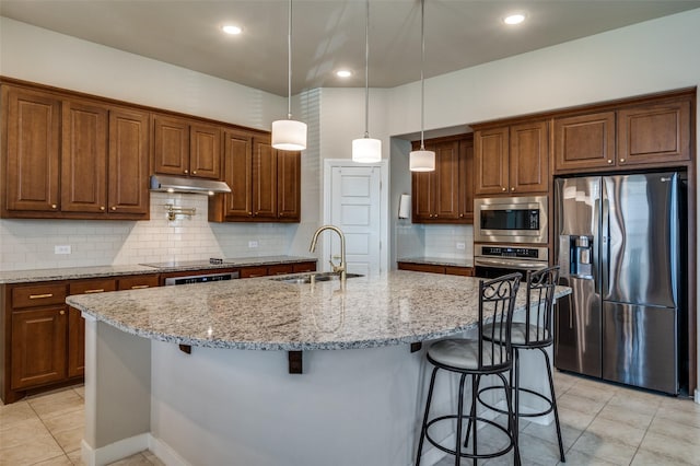 kitchen with light stone counters, a breakfast bar, a sink, stainless steel appliances, and under cabinet range hood