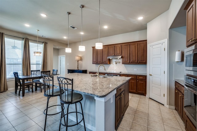 kitchen with wall oven, backsplash, under cabinet range hood, a breakfast bar area, and a sink