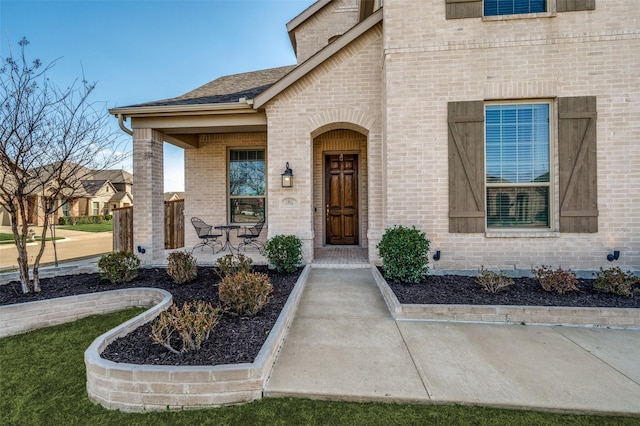 doorway to property with covered porch, brick siding, and a shingled roof