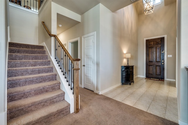 carpeted entrance foyer featuring tile patterned floors, baseboards, stairs, and a towering ceiling