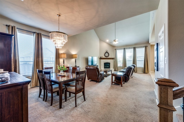 dining space with a glass covered fireplace, high vaulted ceiling, ceiling fan with notable chandelier, and light carpet