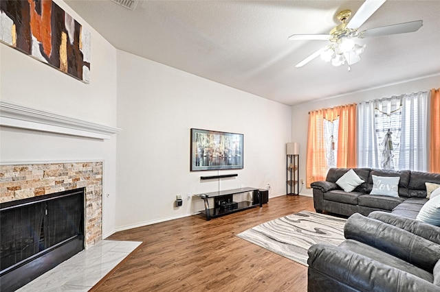 living area with a tile fireplace, ceiling fan, baseboards, and wood finished floors