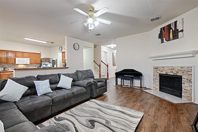 living area with ceiling fan, a fireplace, wood finished floors, visible vents, and stairs