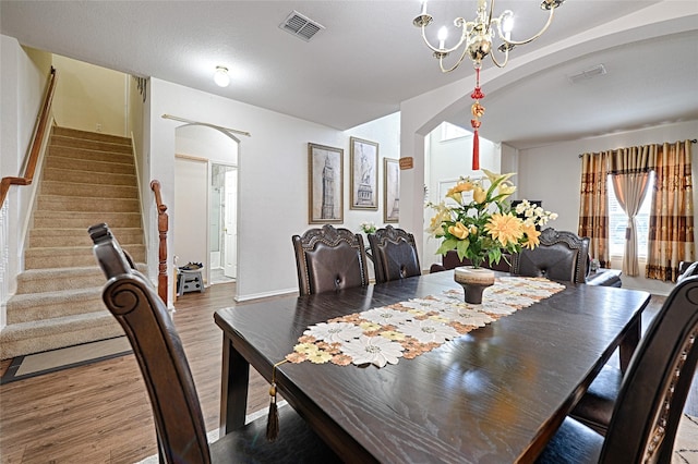 dining space featuring visible vents, arched walkways, wood finished floors, stairs, and a notable chandelier