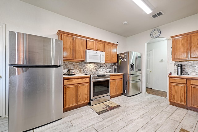 kitchen featuring tasteful backsplash, light countertops, visible vents, light wood-style flooring, and appliances with stainless steel finishes