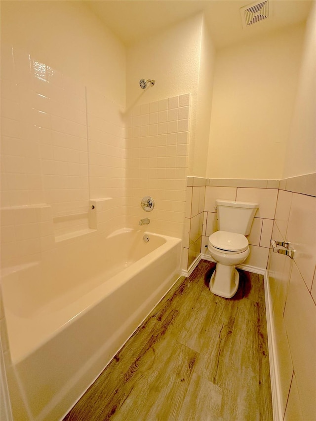 bathroom with toilet, wood finished floors, visible vents, tile walls, and wainscoting