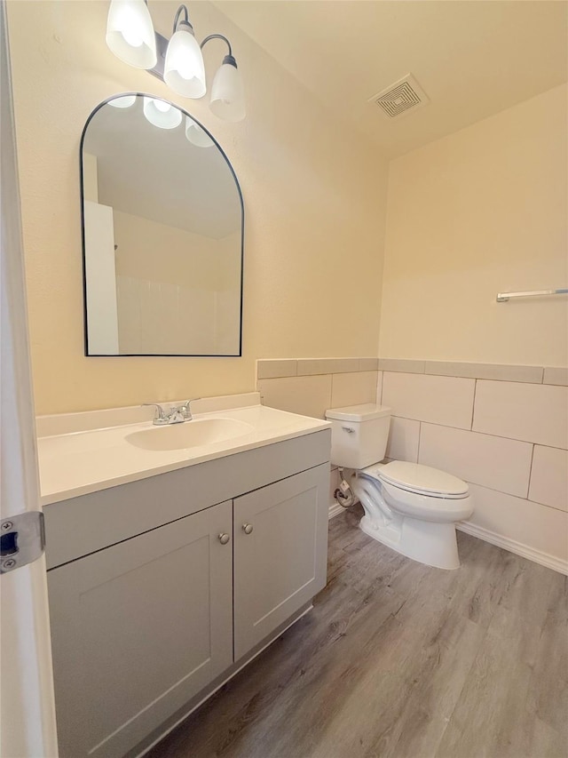 bathroom with toilet, wood finished floors, visible vents, tile walls, and wainscoting