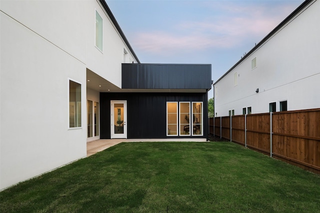 rear view of property with stucco siding, a lawn, and fence