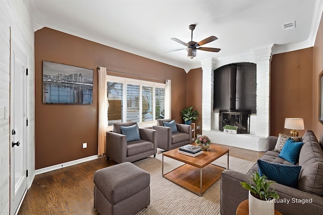 living area featuring a wood stove, ceiling fan, crown molding, and wood finished floors