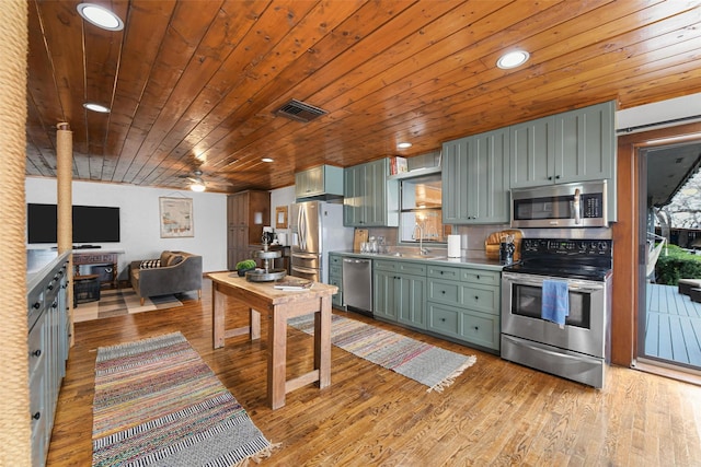 kitchen with recessed lighting, stainless steel appliances, a sink, light wood finished floors, and green cabinetry