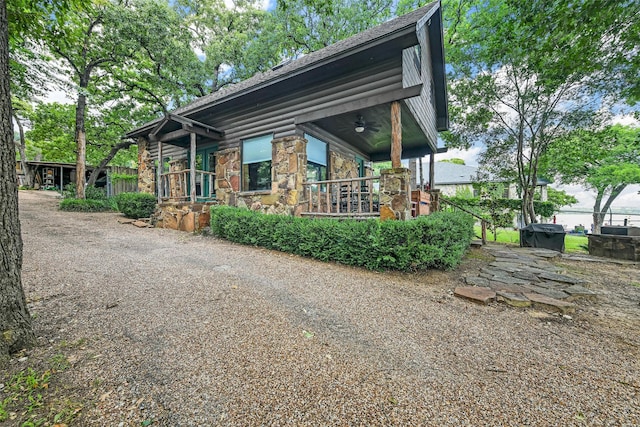 view of front facade featuring a ceiling fan, stone siding, covered porch, and roof with shingles