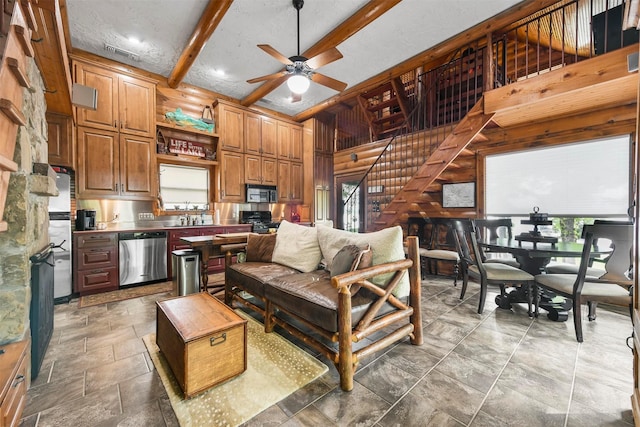 living area with visible vents, ceiling fan, stairway, stone tile flooring, and beam ceiling