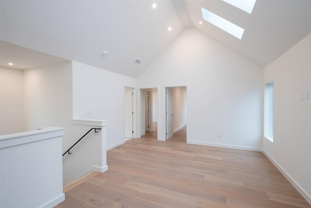 unfurnished room featuring light wood finished floors, visible vents, baseboards, a skylight, and high vaulted ceiling