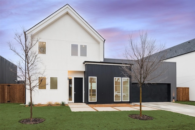 view of front of house featuring an attached garage, fence, stucco siding, a lawn, and driveway