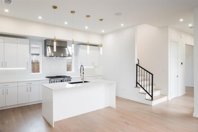 kitchen with light wood-style flooring, a sink, wall chimney range hood, range, and modern cabinets