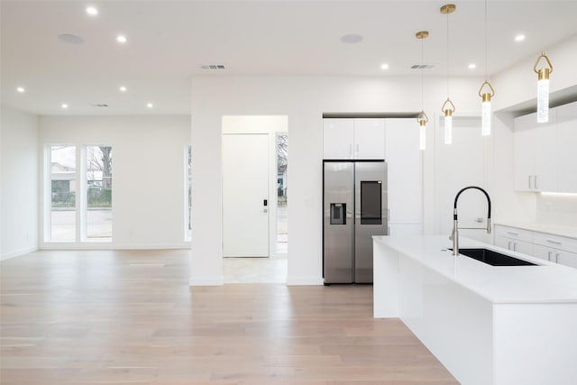 kitchen featuring light wood-style flooring, pendant lighting, stainless steel fridge with ice dispenser, and a sink