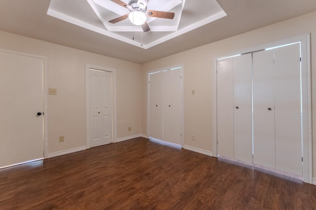 unfurnished bedroom featuring multiple closets, a tray ceiling, baseboards, and wood finished floors