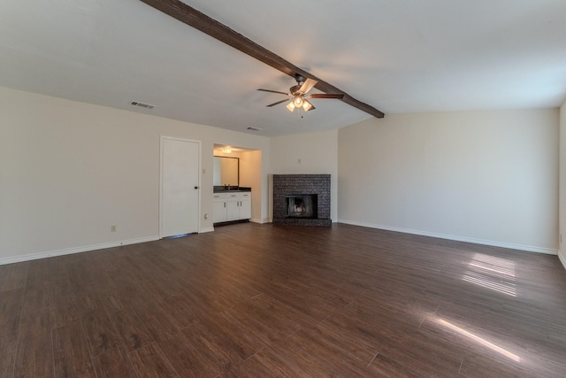 unfurnished living room with visible vents, lofted ceiling with beams, ceiling fan, dark wood-type flooring, and a brick fireplace