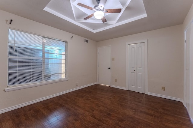 unfurnished room featuring a tray ceiling, visible vents, ceiling fan, wood finished floors, and baseboards