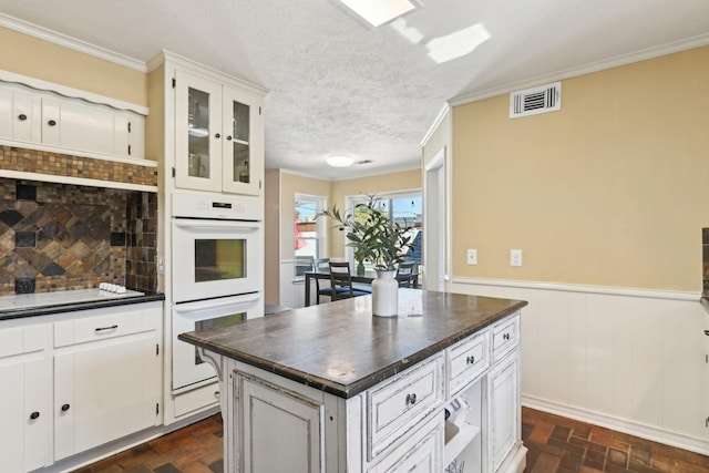 kitchen with visible vents, dark countertops, a wainscoted wall, brick floor, and double oven