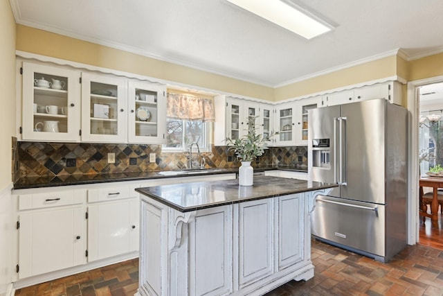 kitchen featuring high end fridge, dark countertops, a sink, and brick floor