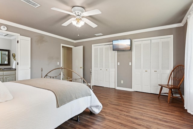 bedroom with wood finished floors, visible vents, baseboards, multiple closets, and ornamental molding